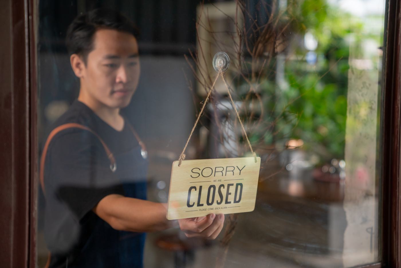 A shop owner turning the sign on his door to Closed