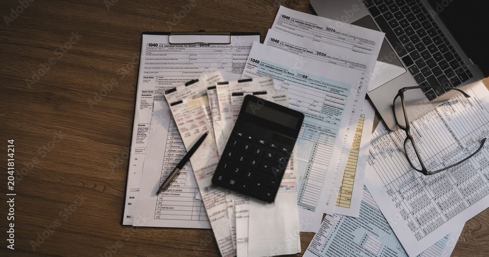 Tax forms, receipts, a calculator and reading glasses spread across a desk